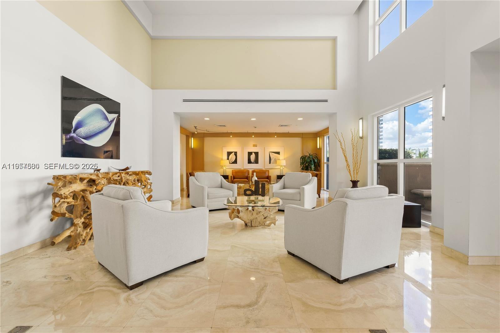 A spacious, high-ceilinged lobby features light-colored armchairs, a glass-topped driftwood table, and marble flooring — 2080 S Ocean Dr # 506, Hallandale Beach FL 33009, HALLANDALE BEACH, FL