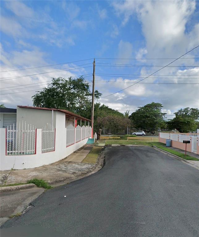 A residential street view shows a white house with a metal fence and utility poles — . 13 UNIT 299, PUNTA SANTIAGO, PR