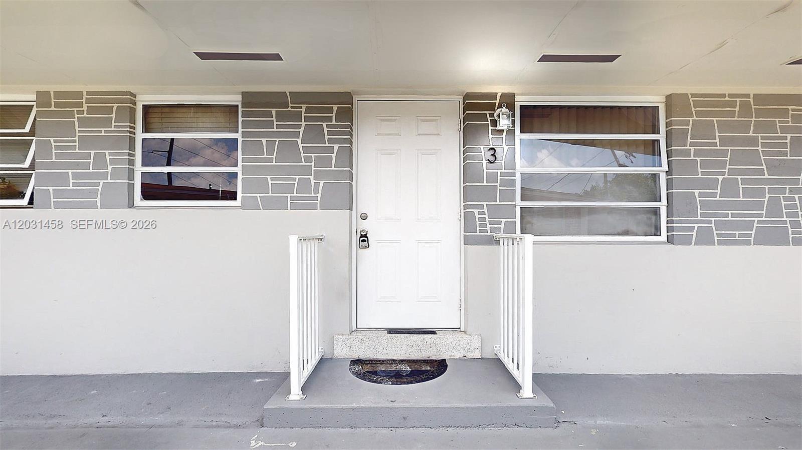 A white front door with a number three sits between two windows and stone-patterned walls — 40 W 10th St # 3, Hialeah FL 33010, HIALEAH, FL