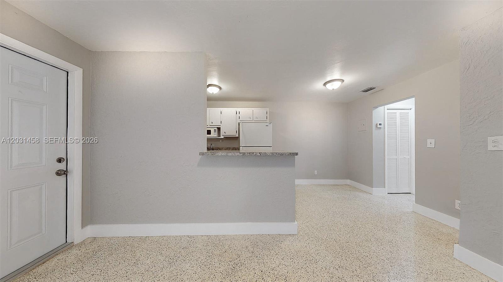 A room with light gray walls, speckled flooring, a kitchen pass-through, and a white door — 40 W 10th St # 3, Hialeah FL 33010, HIALEAH, FL