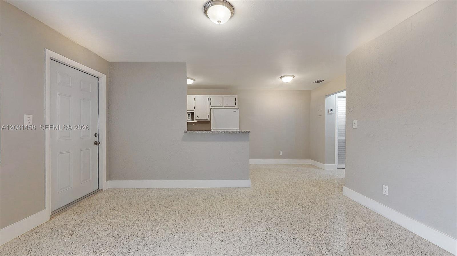 An open-concept living area features light gray walls, speckled flooring, and a pass-through kitchen — 40 W 10th St # 3, Hialeah FL 33010, HIALEAH, FL