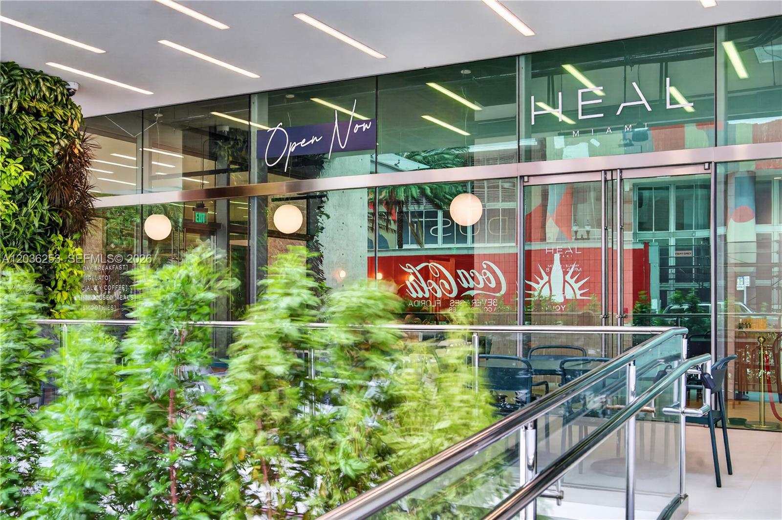 The exterior of a modern storefront features glass walls, a green wall, and outdoor seating — 2 S Biscayne Blvd, Miami FL 33131, MIAMI, FL