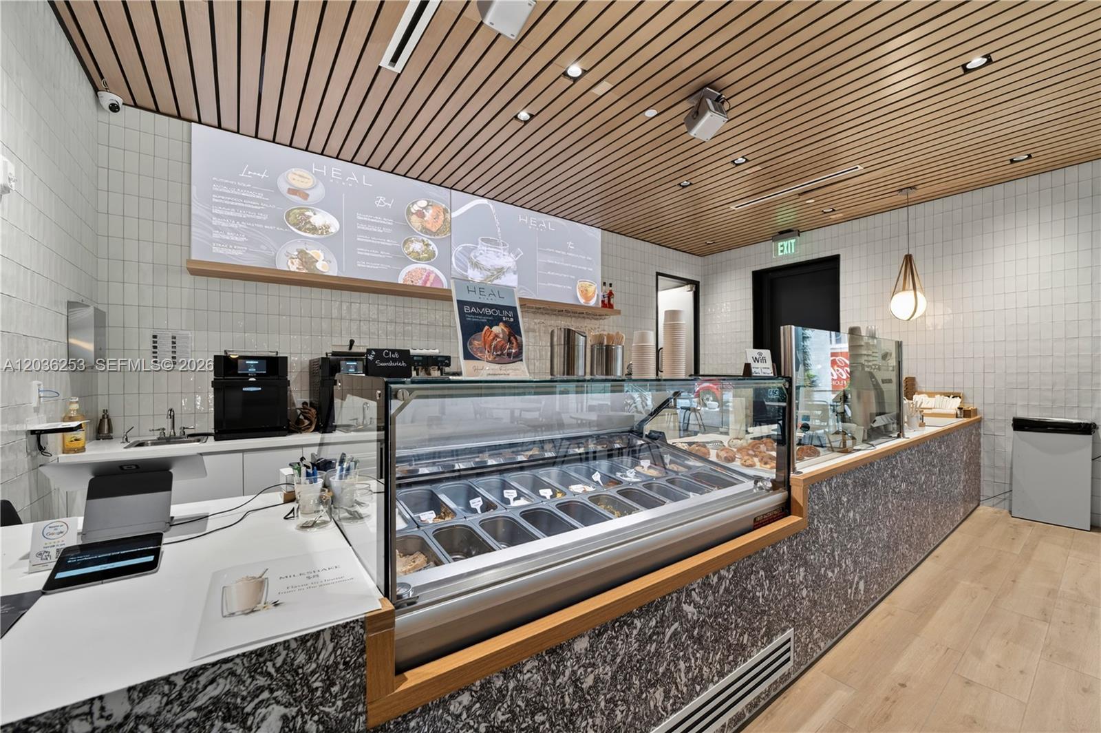 A modern cafe interior features a glass display case, marble-patterned counters, and wood-slat ceilings — 2 S Biscayne Blvd, Miami FL 33131, MIAMI, FL
