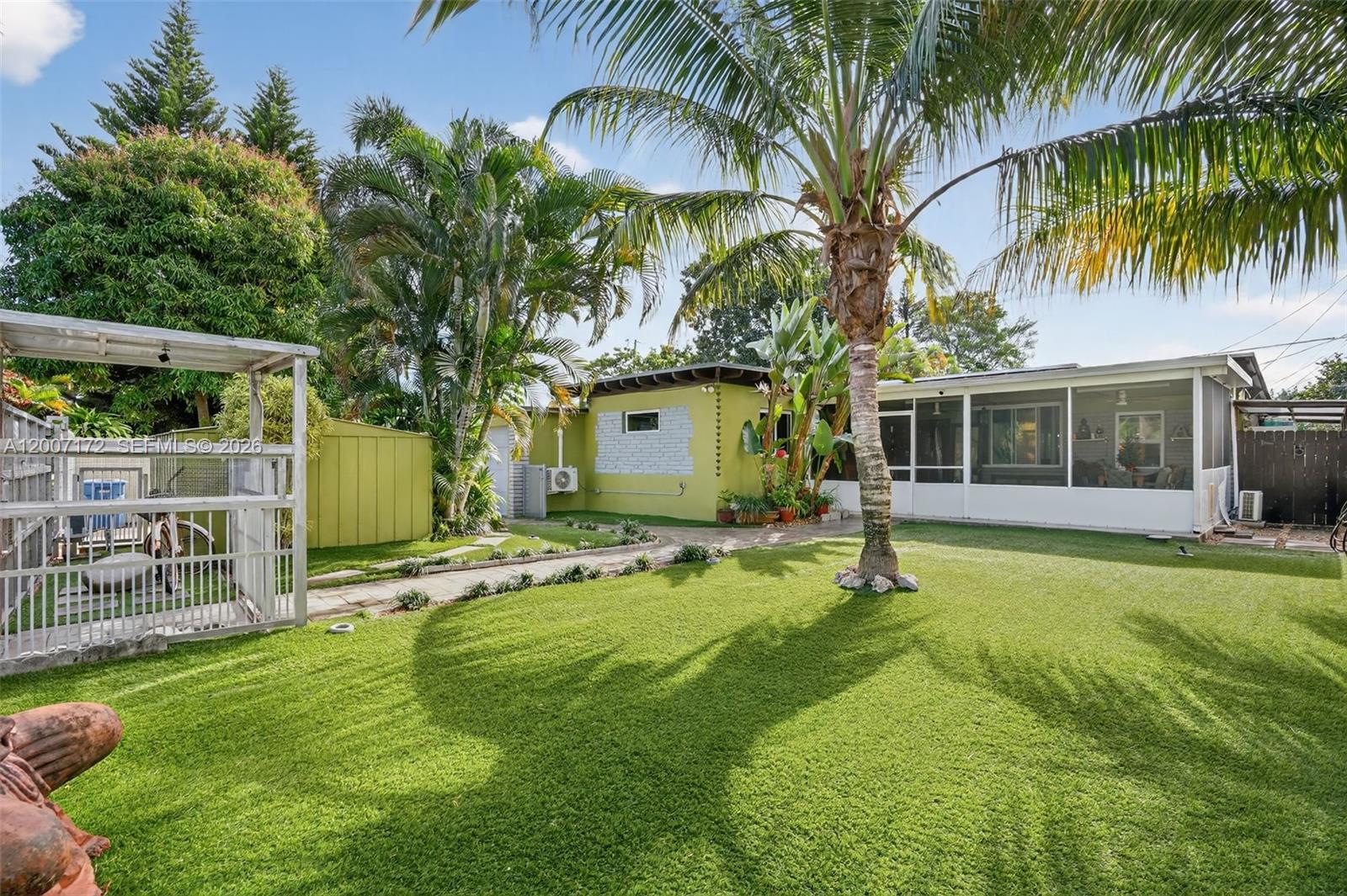 A backyard features a green house with a screened porch, palm trees, and a lawn — 270 NW 106th St, Miami FL 33150, MIAMI, FL
