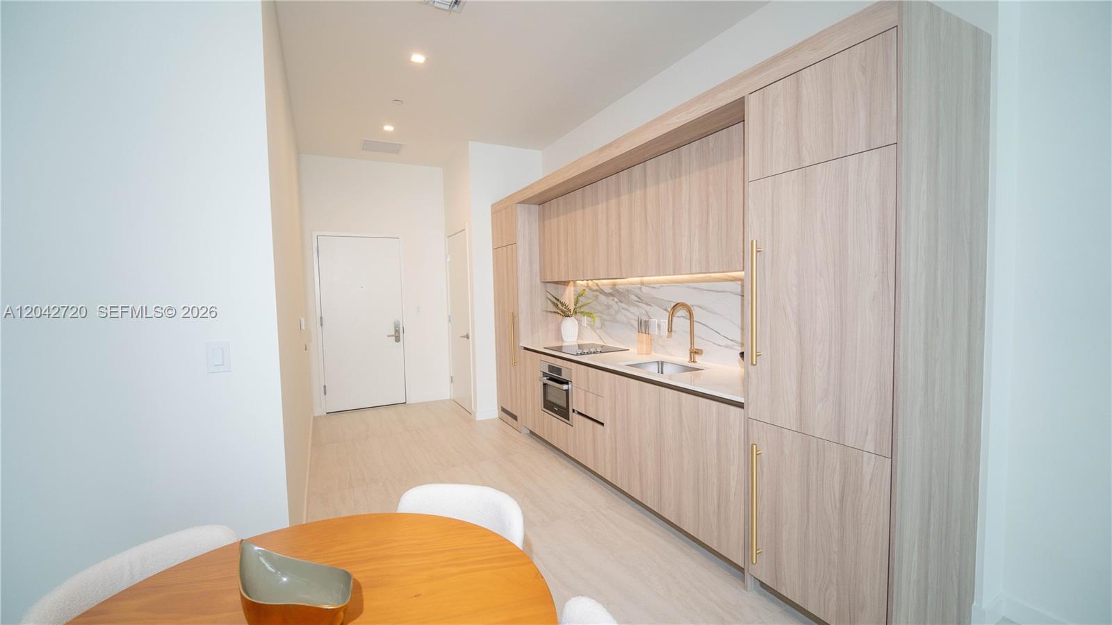 A modern kitchen features light wood cabinetry, a marble backsplash, and a gold faucet — 77 SE 5th St # 311, Miami FL 33131, MIAMI, FL