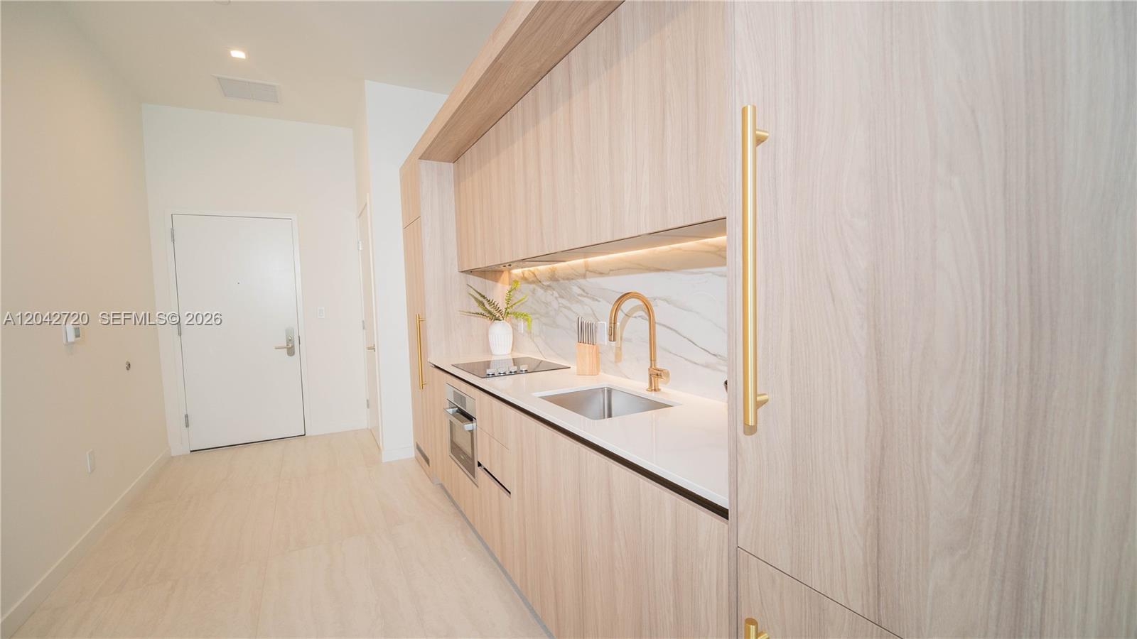 A modern kitchen features light wood cabinetry, gold hardware, and a white marble backsplash — 77 SE 5th St # 311, Miami FL 33131, MIAMI, FL