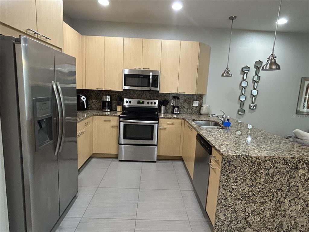 A kitchen features light wood cabinets, granite countertops, stainless steel appliances, and gray tile flooring — 1421 RETREAT CIRCLE, CLERMONT, FL