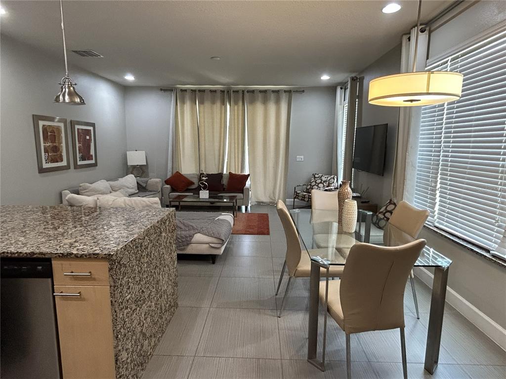 An open-concept living and dining area features tile flooring, granite countertops, and neutral furnishings — 1421 RETREAT CIRCLE, CLERMONT, FL