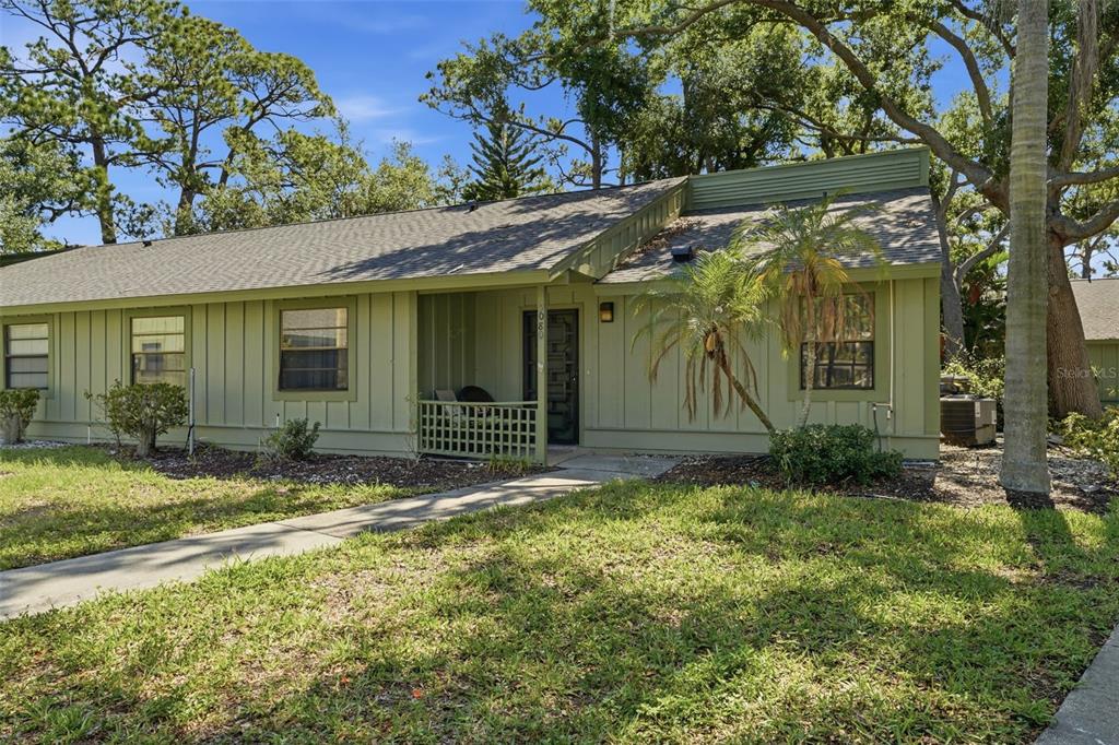 A single-story green house with a front porch, walkway, and surrounding trees — 5080 BARRINGTON CIRCLE UNIT 3102, SARASOTA, FL