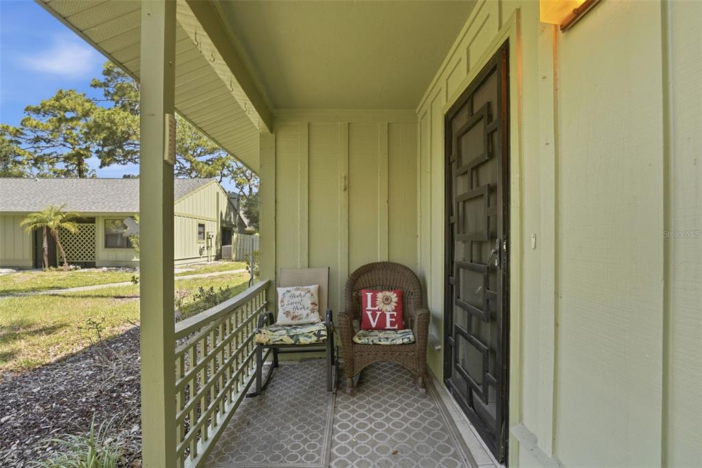 A covered porch features light green siding, two chairs, and a decorative metal screen door — 5080 BARRINGTON CIRCLE UNIT 3102, SARASOTA, FL