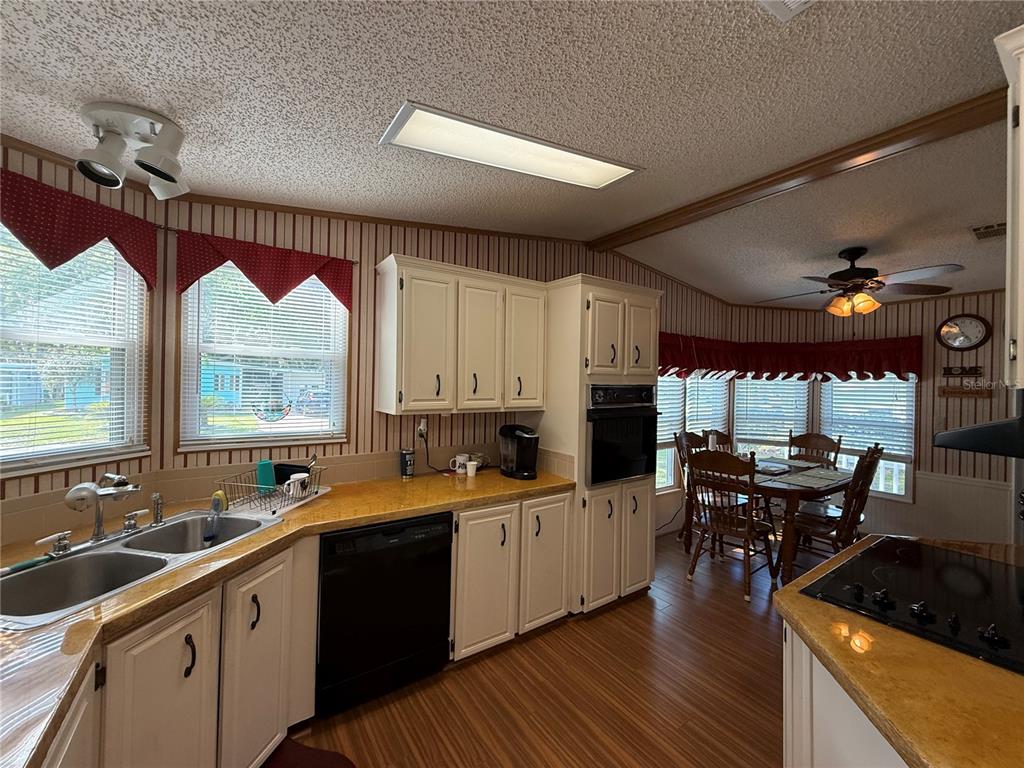 A kitchen with white cabinets, yellow countertops, a black dishwasher, and an adjacent dining area — 807 OAK BOULEVARD, WILDWOOD, FL