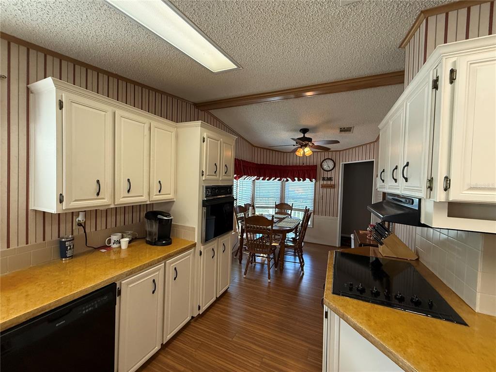 A kitchen with white cabinets, yellow countertops, and striped wallpaper leads to a dining area — 807 OAK BOULEVARD, WILDWOOD, FL