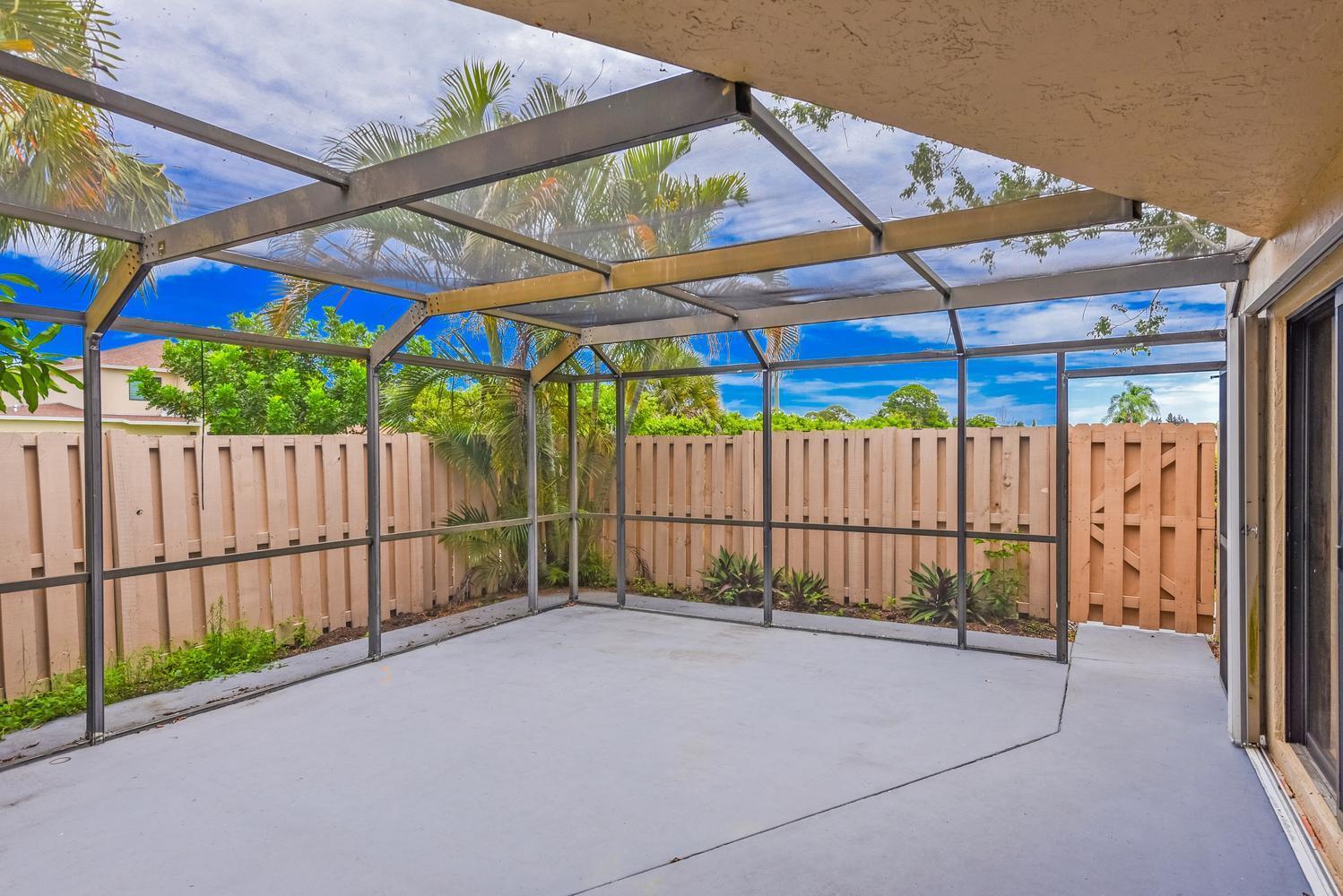 A screened-in patio with a concrete floor, metal framing, and a wooden privacy fence — 3640 Village Drive # A, Delray Beach FL 33445, DELRAY BEACH, FL