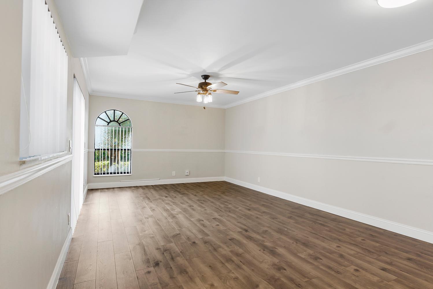 An empty room features wood-look flooring, a ceiling fan, and an arched window — 3640 Village Drive # A, Delray Beach FL 33445, DELRAY BEACH, FL