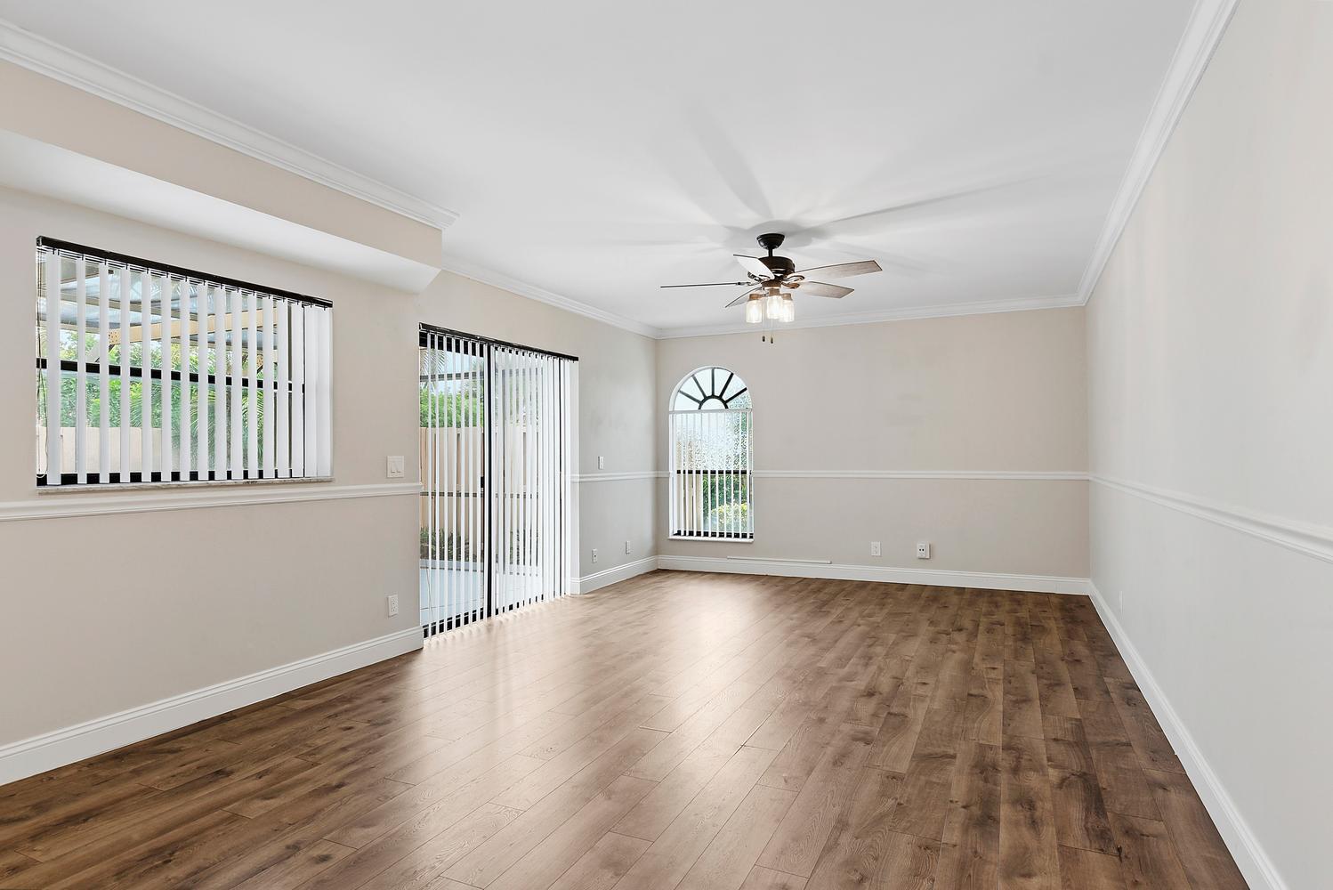 An empty room features wood-look flooring, a ceiling fan, vertical blinds, and an arched window — 3640 Village Drive # A, Delray Beach FL 33445, DELRAY BEACH, FL