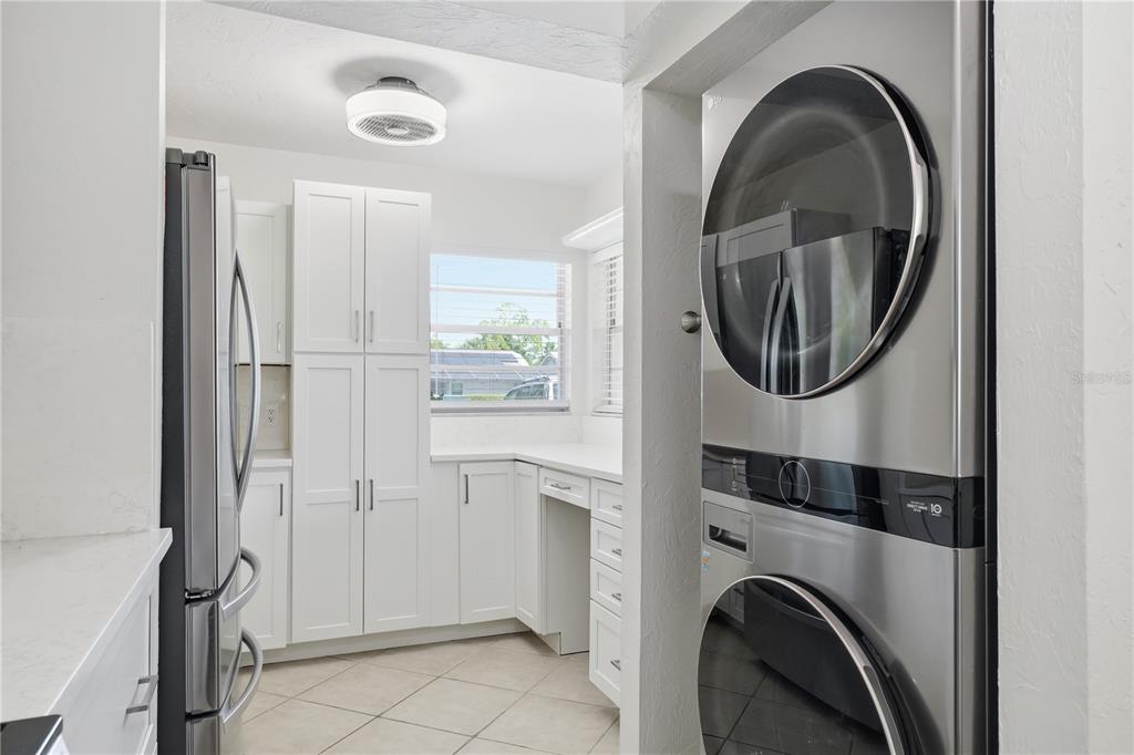 A laundry area with a stacked washer and dryer next to a white-cabinet kitchen — 7860 PALM AIRE LANE UNIT 103, SARASOTA, FL