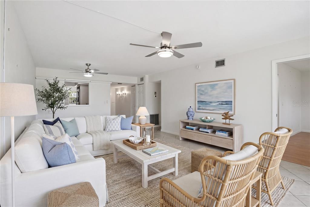 A bright living room features a white sectional sofa, rattan chairs, and two ceiling fans — 7860 PALM AIRE LANE UNIT 103, SARASOTA, FL