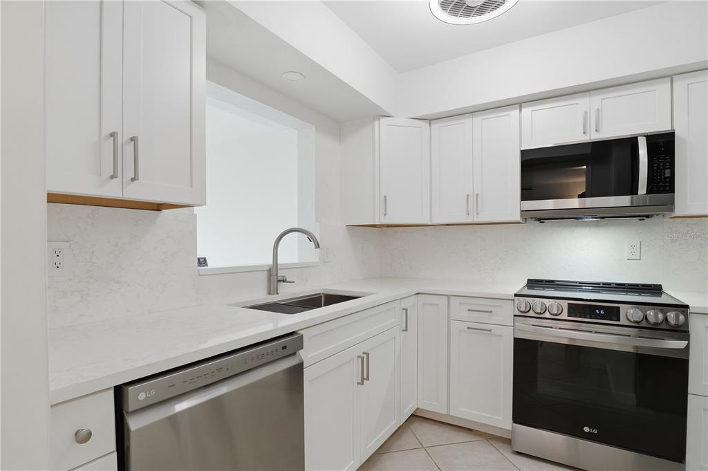 A kitchen features white cabinets, stainless steel appliances, and light-colored quartz countertops — 7860 PALM AIRE LANE UNIT 103, SARASOTA, FL