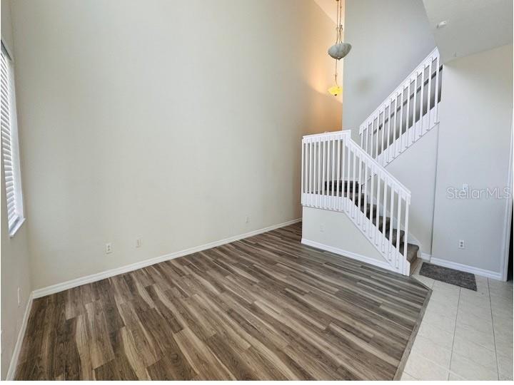 An empty room features wood-look flooring, a high ceiling, and a white staircase with railings — 6114 CHAPLEDALE DRIVE, ORLANDO, FL