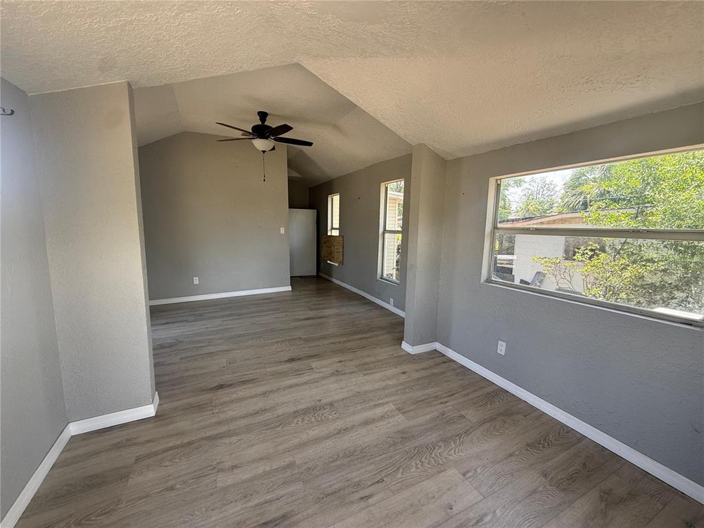 An empty room features gray walls, light wood-look flooring, a vaulted ceiling, and large windows — 2220 20TH STREET S, ST PETERSBURG, FL