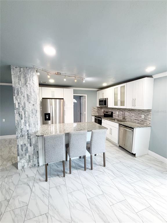A kitchen features white cabinets, granite countertops, a stone-tiled pillar, and light-colored marble-look flooring — 3427 16TH AVENUE S, ST PETERSBURG, FL