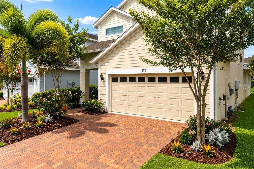 A beige house with a brick driveway, a two-car garage, and landscaped front gardens — 6118 VOYAGERS PLACE, APOLLO BEACH, FL