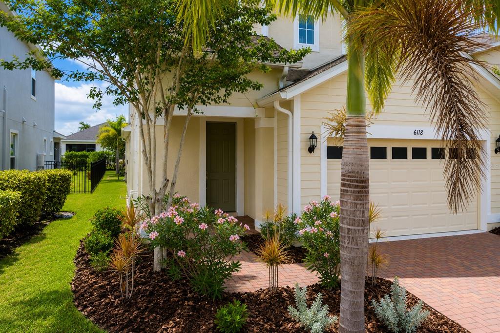 A yellow house exterior features a brick driveway, a front entrance, and a palm tree — 6118 VOYAGERS PLACE, APOLLO BEACH, FL