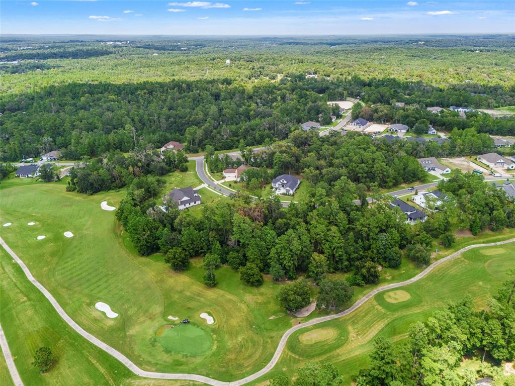 An aerial view shows houses nestled in a wooded area adjacent to a golf course — 5979 CREEK RIDGE ROAD, BROOKSVILLE, FL