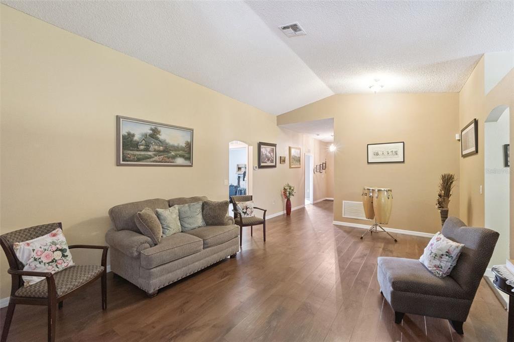 A living room with wood-look flooring, a sofa, two armchairs, and a pair of congas — 1504 FORT MEADE PLACE, KISSIMMEE, FL