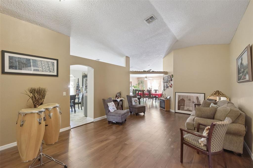 A living room with wood-look flooring, vaulted ceilings, and a view into the dining area — 1504 FORT MEADE PLACE, KISSIMMEE, FL