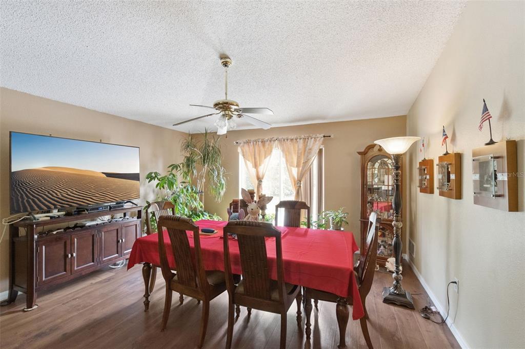 A dining room features a red-clothed table, wooden chairs, a television, and a ceiling fan — 1504 FORT MEADE PLACE, KISSIMMEE, FL