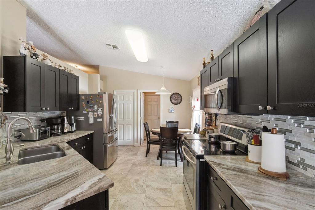 A kitchen features dark cabinets, stone-patterned countertops, stainless steel appliances, and a dining area — 1504 FORT MEADE PLACE, KISSIMMEE, FL