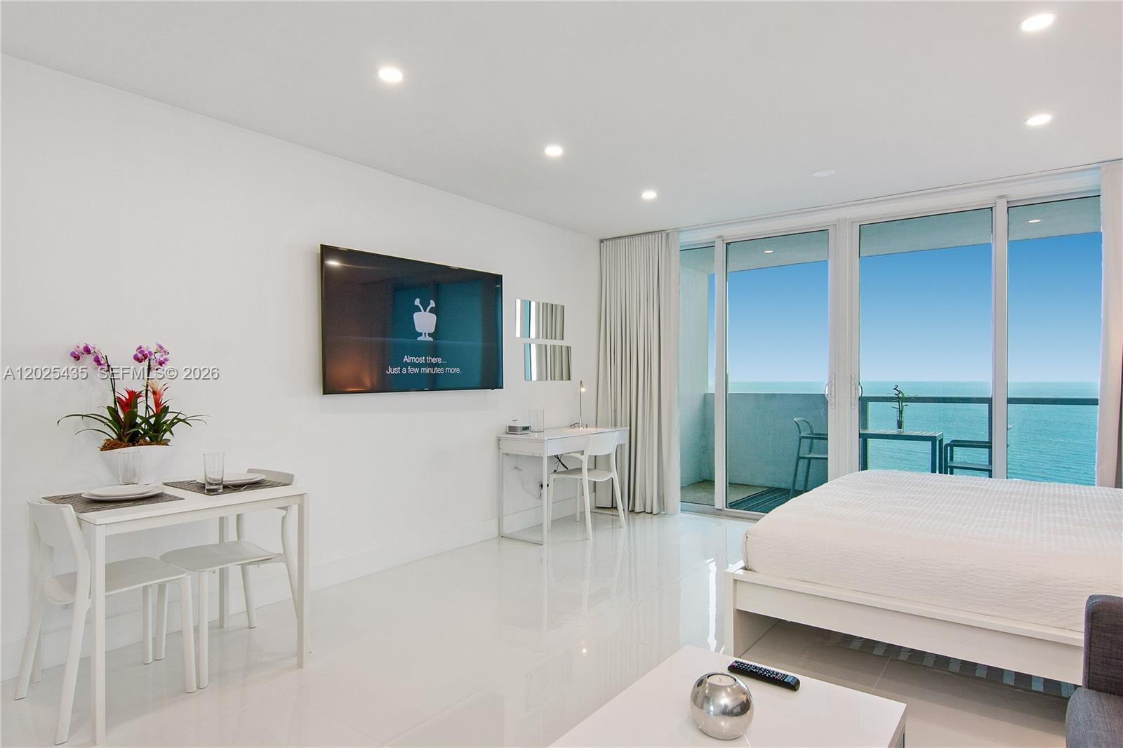 A bright, modern bedroom features white tile floors, a wall-mounted television, and ocean views — 5445 Collins av, Miami Beach FL 33140, MIAMI BEACH, FL