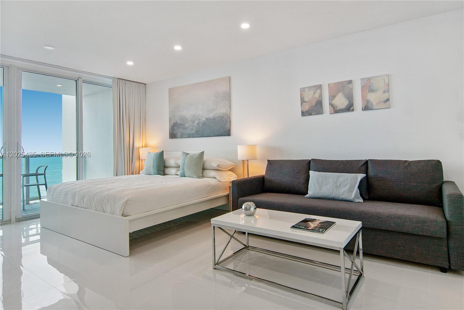 A modern studio room features a bed, a dark sofa, and a balcony with ocean views — 5445 Collins av, Miami Beach FL 33140, MIAMI BEACH, FL