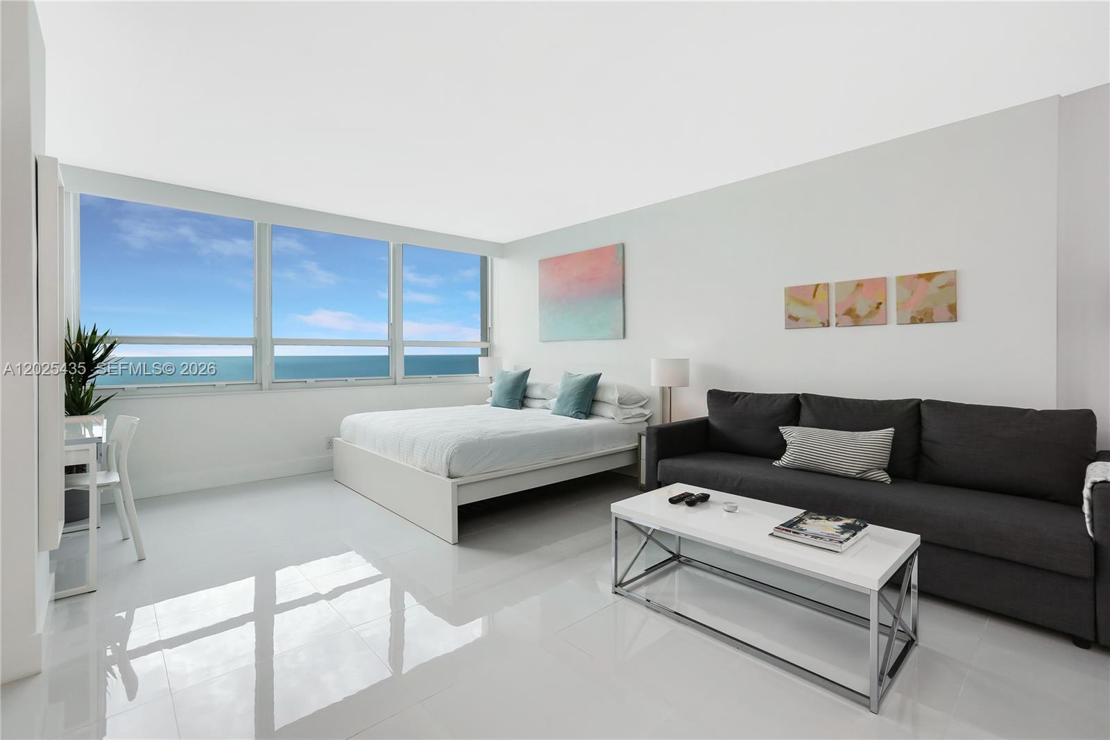 A bedroom with a white bed, dark sofa, and large windows overlooking the ocean — 5445 Collins av, Miami Beach FL 33140, MIAMI BEACH, FL