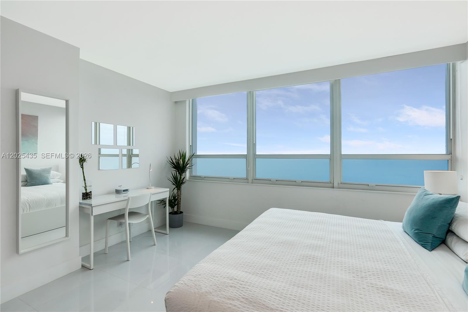 A bright bedroom features white furniture, a desk, a mirror, and floor-to-ceiling ocean views — 5445 Collins av, Miami Beach FL 33140, MIAMI BEACH, FL