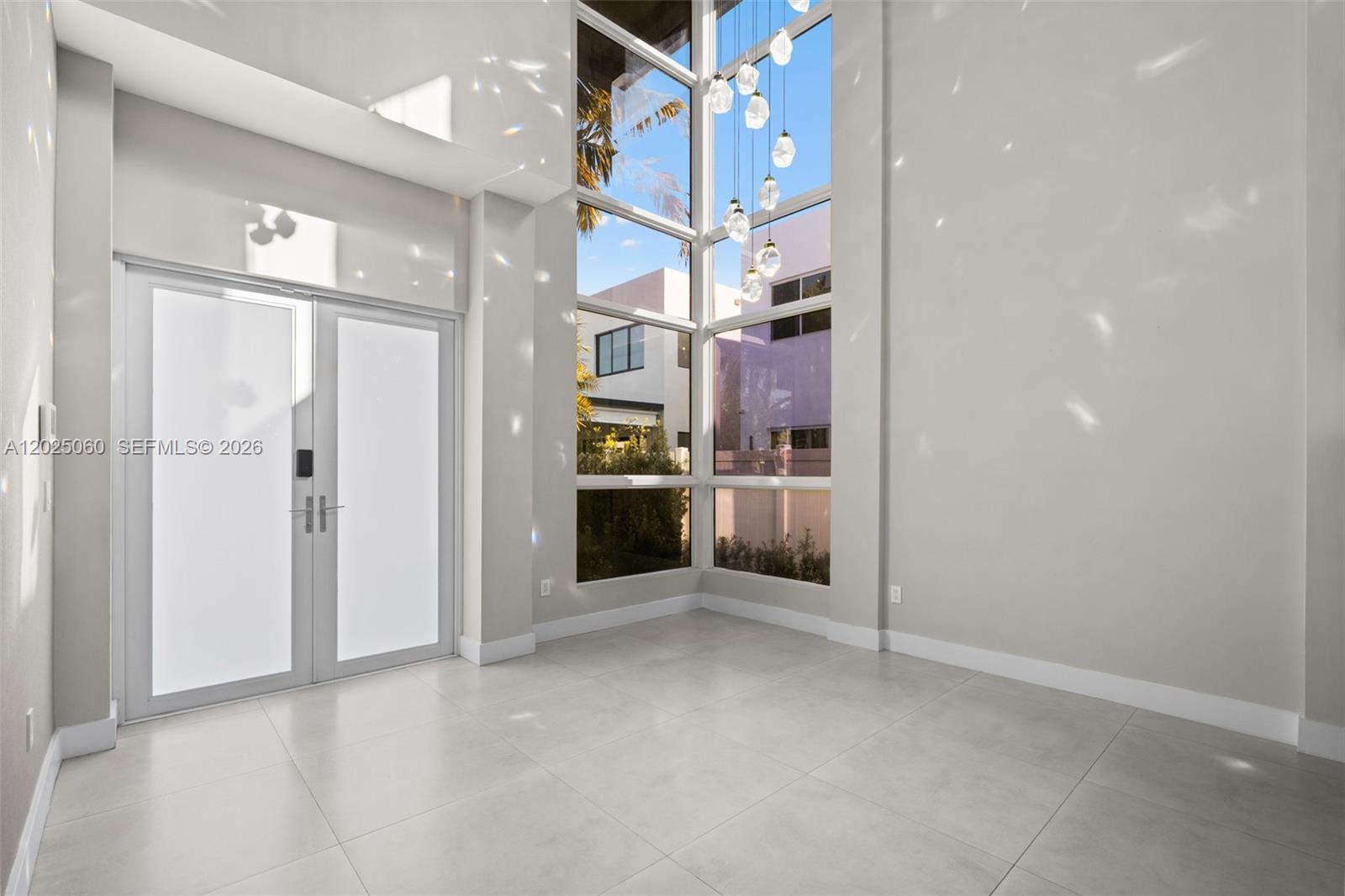 A bright, modern entryway features large floor-to-ceiling windows, light tile flooring, and hanging pendant lights — 7534 NW 98th Ave, Doral FL 33178, DORAL, FL
