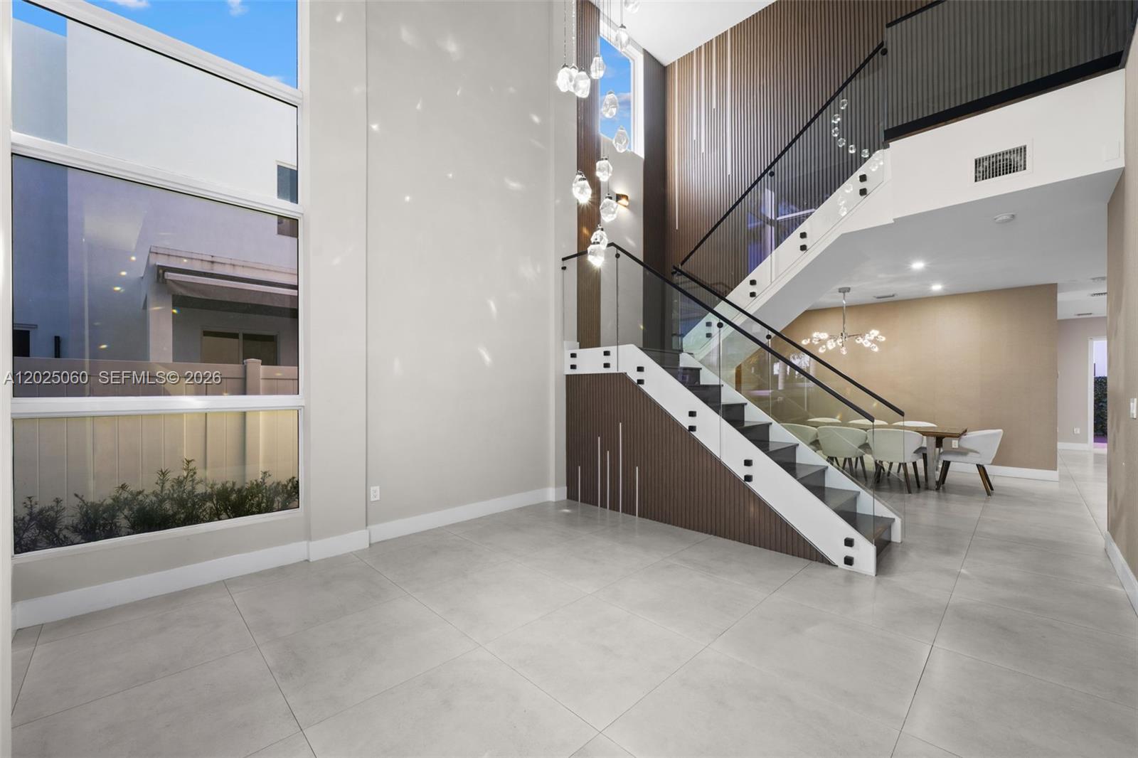 A modern foyer features a glass-railed staircase, wood-slat wall paneling, and a tall chandelier — 7534 NW 98th Ave, Doral FL 33178, DORAL, FL