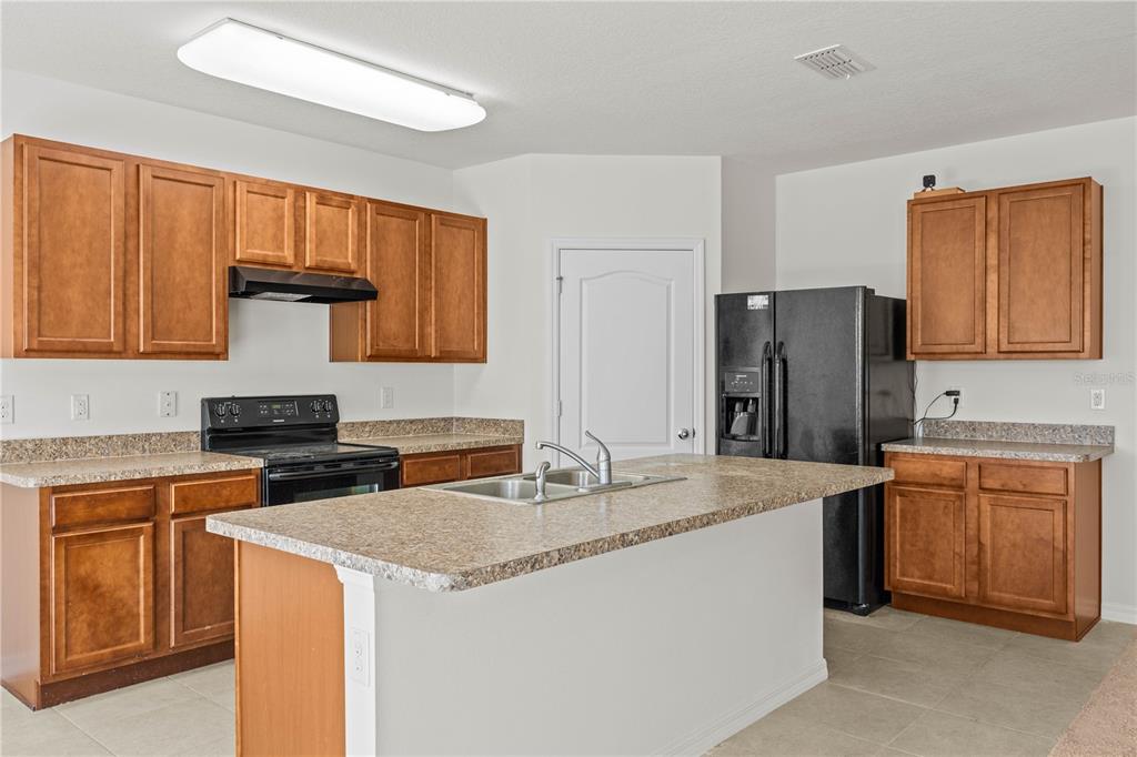 A kitchen features wood cabinets, laminate countertops, a center island, and black appliances — 817 SHEEN CIRCLE, HAINES CITY, FL