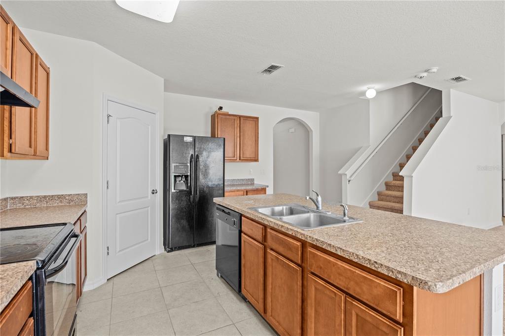 A kitchen features wood cabinets, laminate countertops, a black refrigerator, and a staircase nearby — 817 SHEEN CIRCLE, HAINES CITY, FL