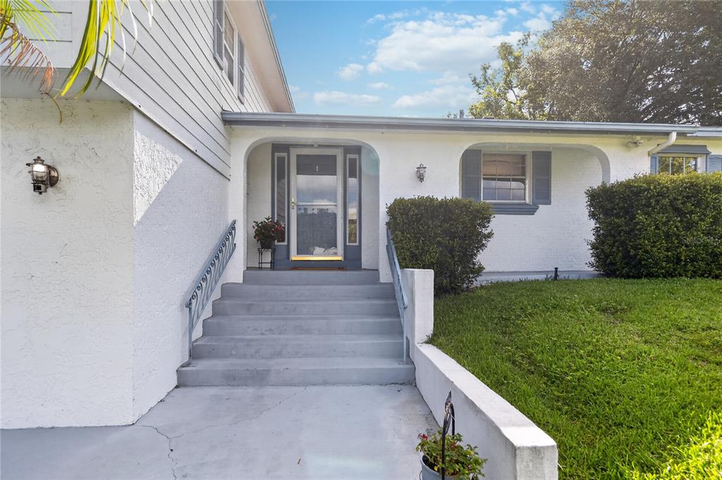 A white house exterior features a concrete staircase leading to a front door under an archway — 656 LITTLE WEKIVA ROAD, ALTAMONTE SPRINGS, FL