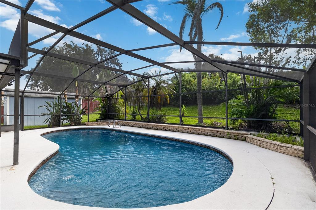 A kidney-shaped swimming pool sits inside a screened-in enclosure with a stone retaining wall — 656 LITTLE WEKIVA ROAD, ALTAMONTE SPRINGS, FL
