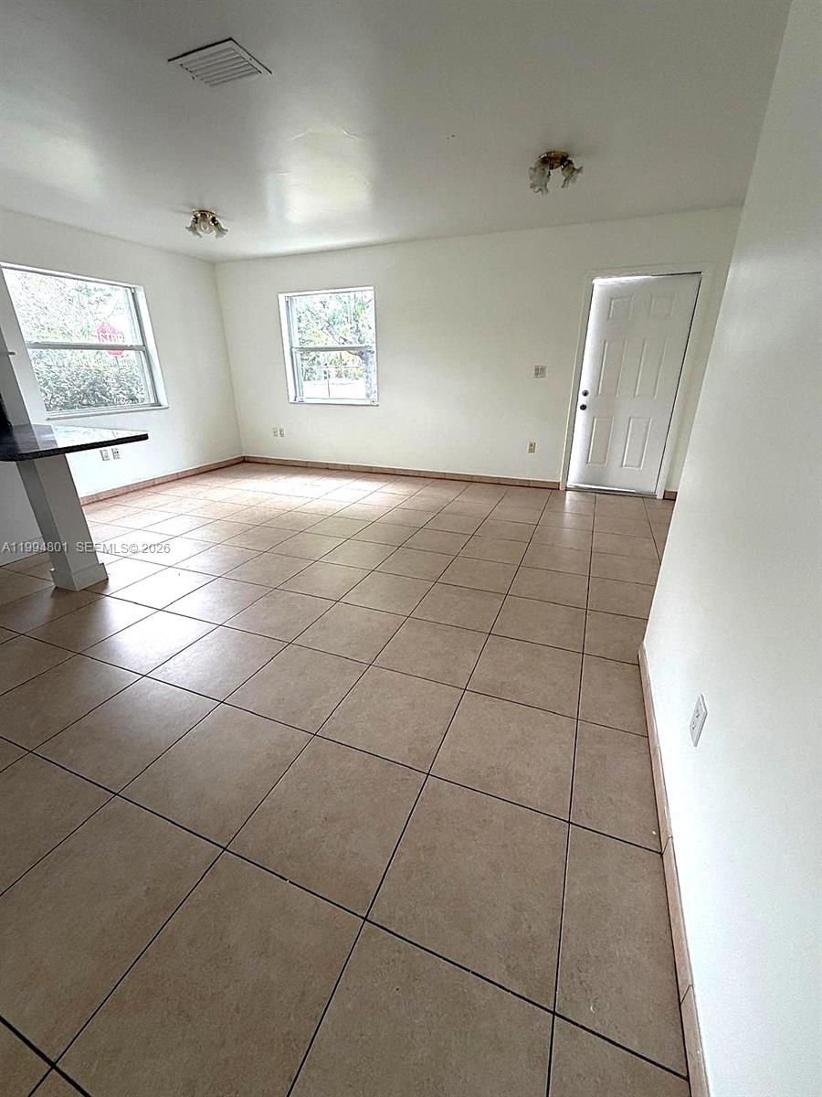 An empty room features beige tile flooring, white walls, two windows, and a white door — 14140 NE 2 Ct # 4, Miami FL 33161, MIAMI, FL
