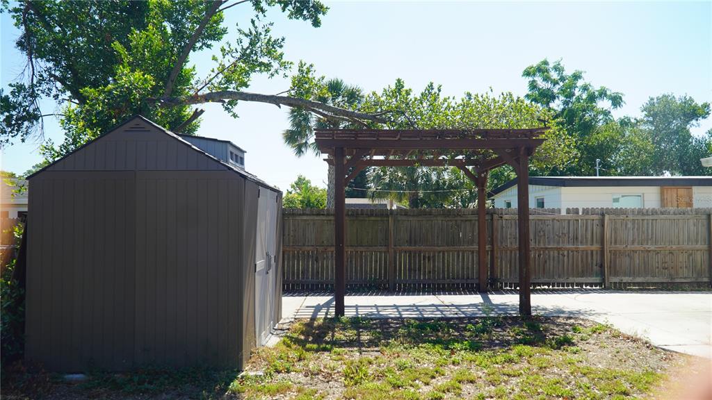 A backyard features a brown storage shed, a wooden pergola, and a wooden privacy fence — 4111 W MONTGOMERY TERRACE, TAMPA, FL