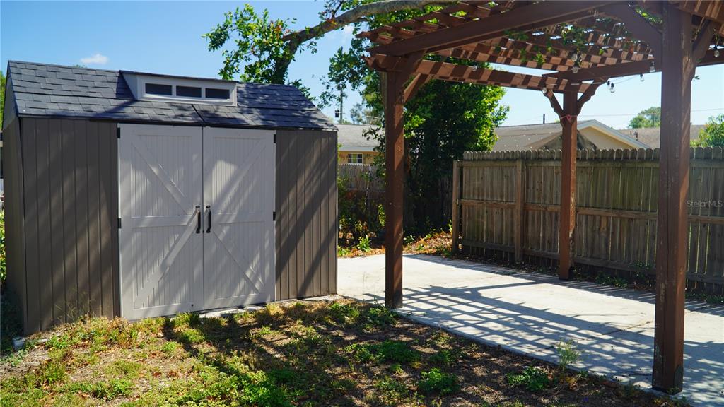A backyard features a storage shed with double doors next to a wooden pergola structure — 4111 W MONTGOMERY TERRACE, TAMPA, FL