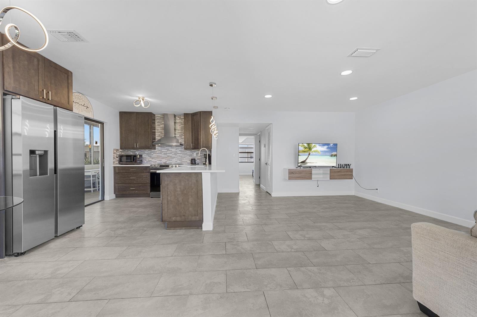 A kitchen with stainless steel appliances and a floating media console in an open-concept room — 234 Capri E, Delray Beach FL 33484, DELRAY BEACH, FL