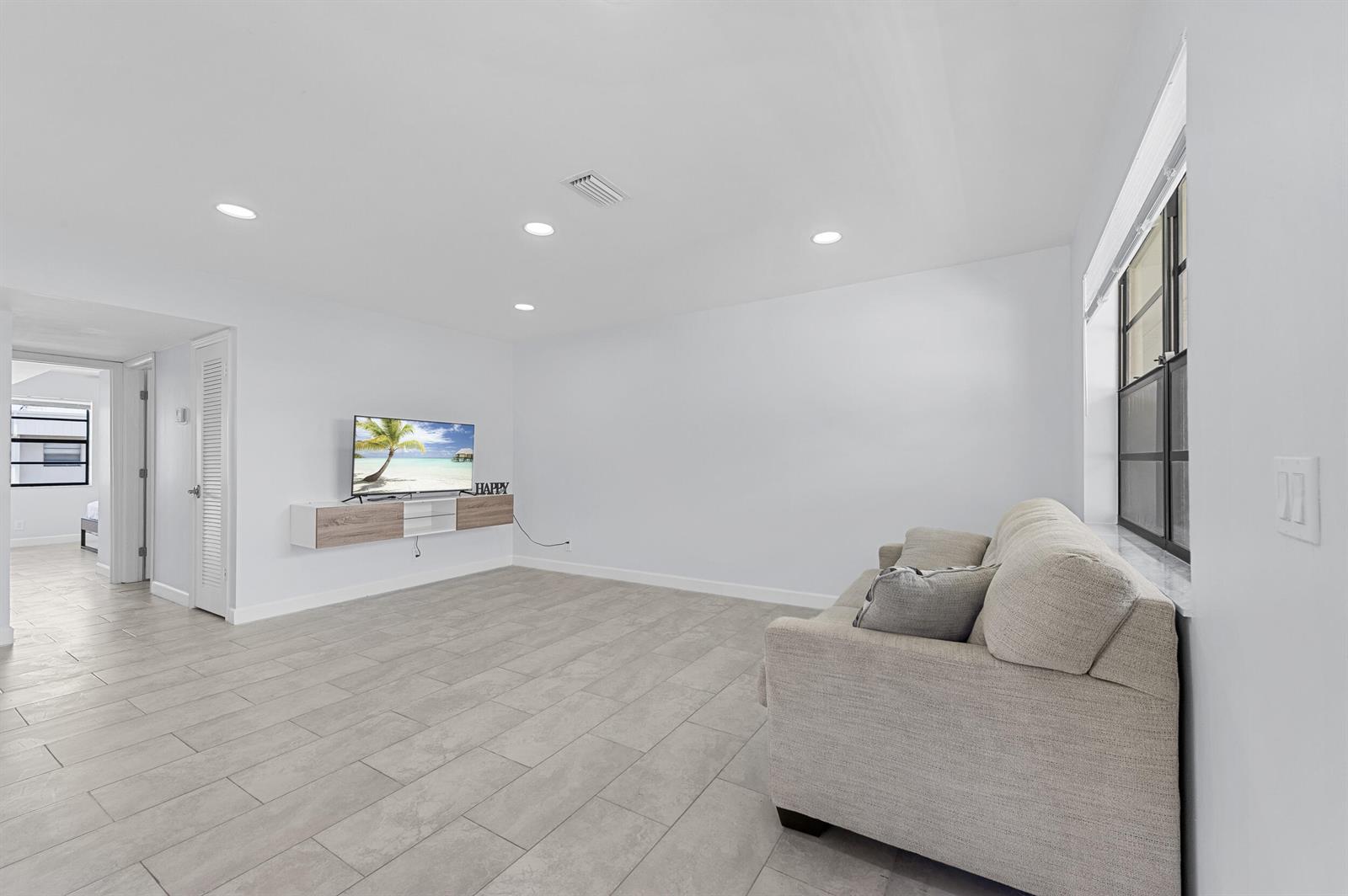 A living room features light gray tile flooring, white walls, a floating media console, and a sofa — 234 Capri E, Delray Beach FL 33484, DELRAY BEACH, FL