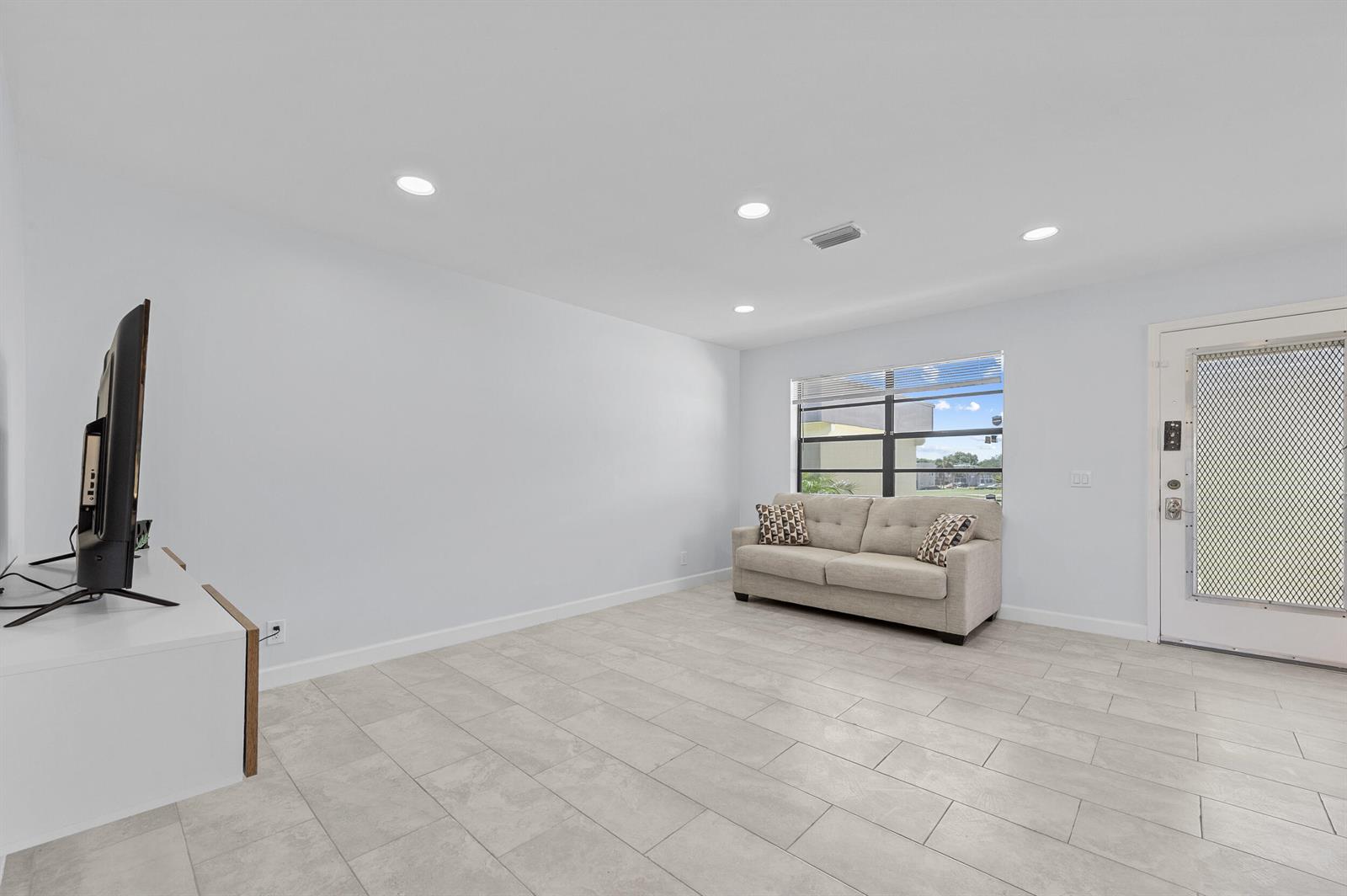 A living room features light gray tile flooring, a beige sofa, and a television stand — 234 Capri E, Delray Beach FL 33484, DELRAY BEACH, FL