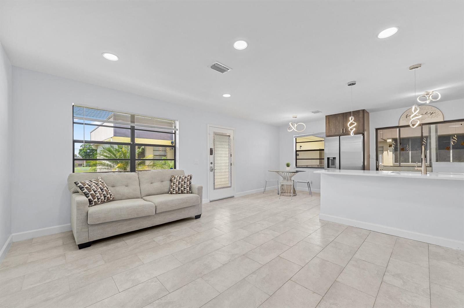 An open-concept living and dining area features light tile flooring, a sofa, and kitchen island — 234 Capri E, Delray Beach FL 33484, DELRAY BEACH, FL
