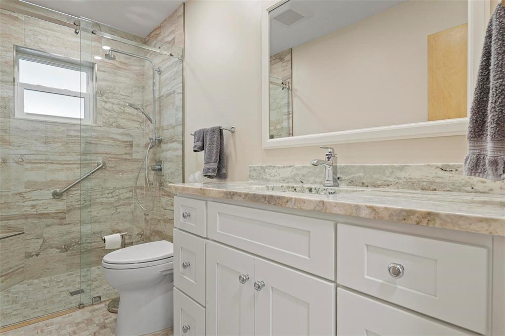 A bathroom features a white vanity with a stone countertop, a mirror, and a glass-enclosed shower — 1040 COCKRILL STREET, VENICE, FL